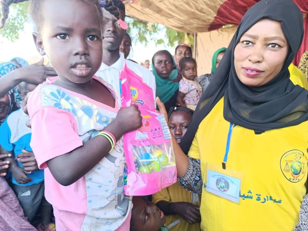 A young Sudanese girl receiving a relief package from a GlobalNetPD volunteer during a humanitarian distribution event.